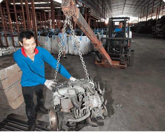 Staff lifting a used engine with a chain hoist